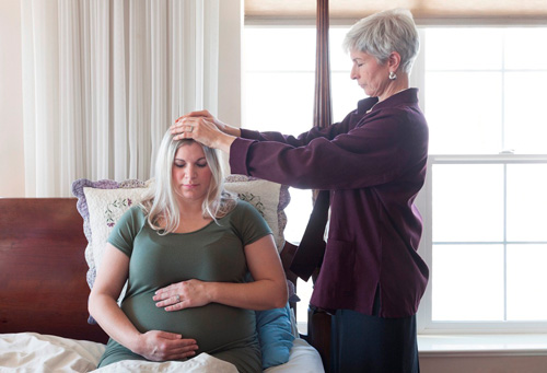 A woman giving a blessing to a pregnant woman.